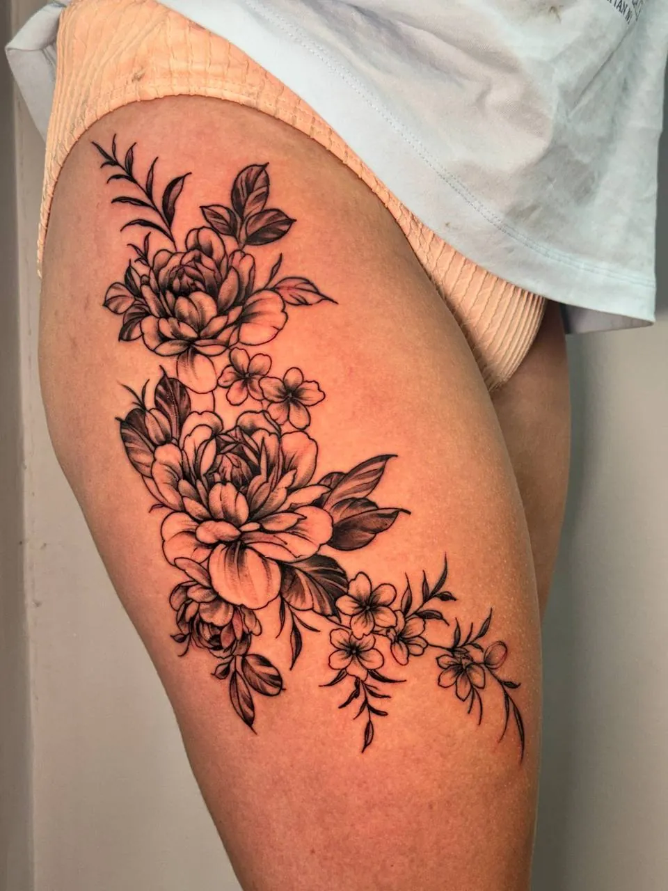 Black and grey tattoo of peonies and small blossoms on the thigh