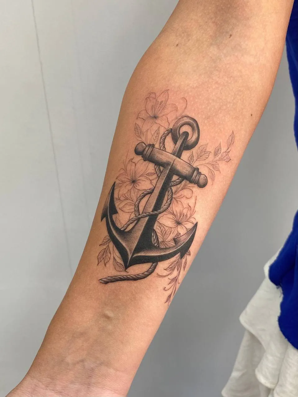 Black and grey anchor surrounded by flowers on the forearm