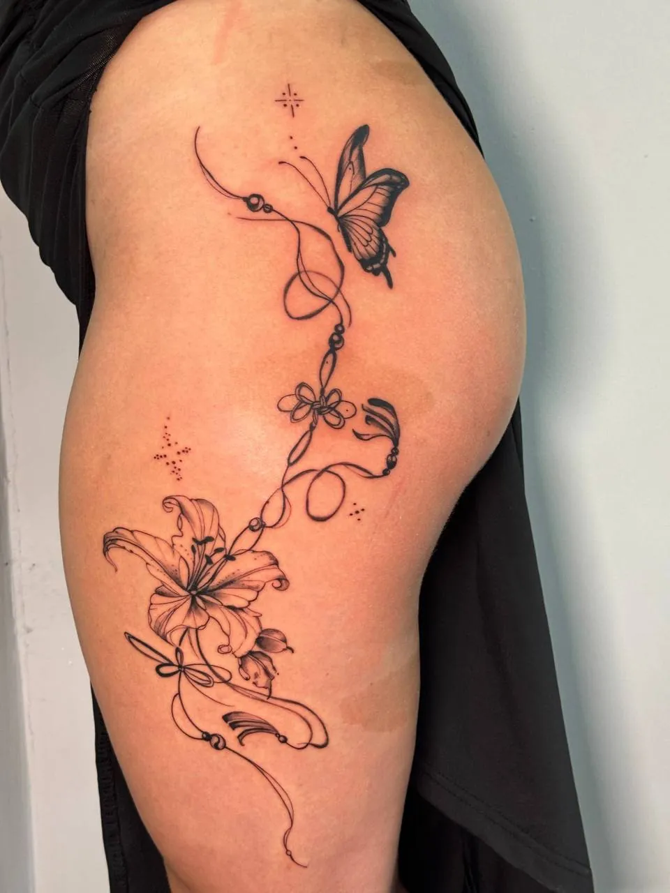 Fine-line butterfly and a lily with buds on a flowing ribbon along the hip
