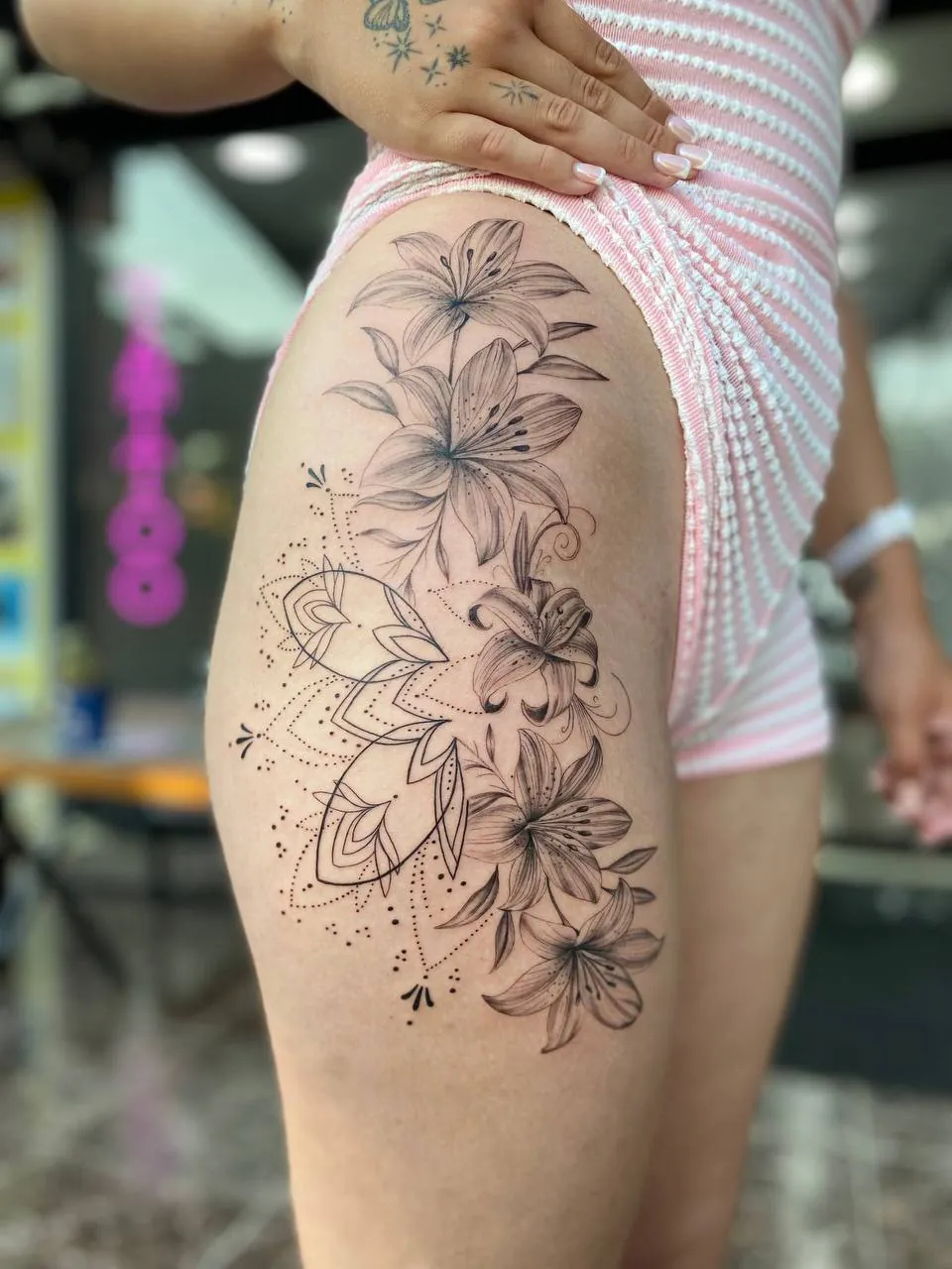 Ornamental tattoo of lilies over a dotwork mandala on the hip