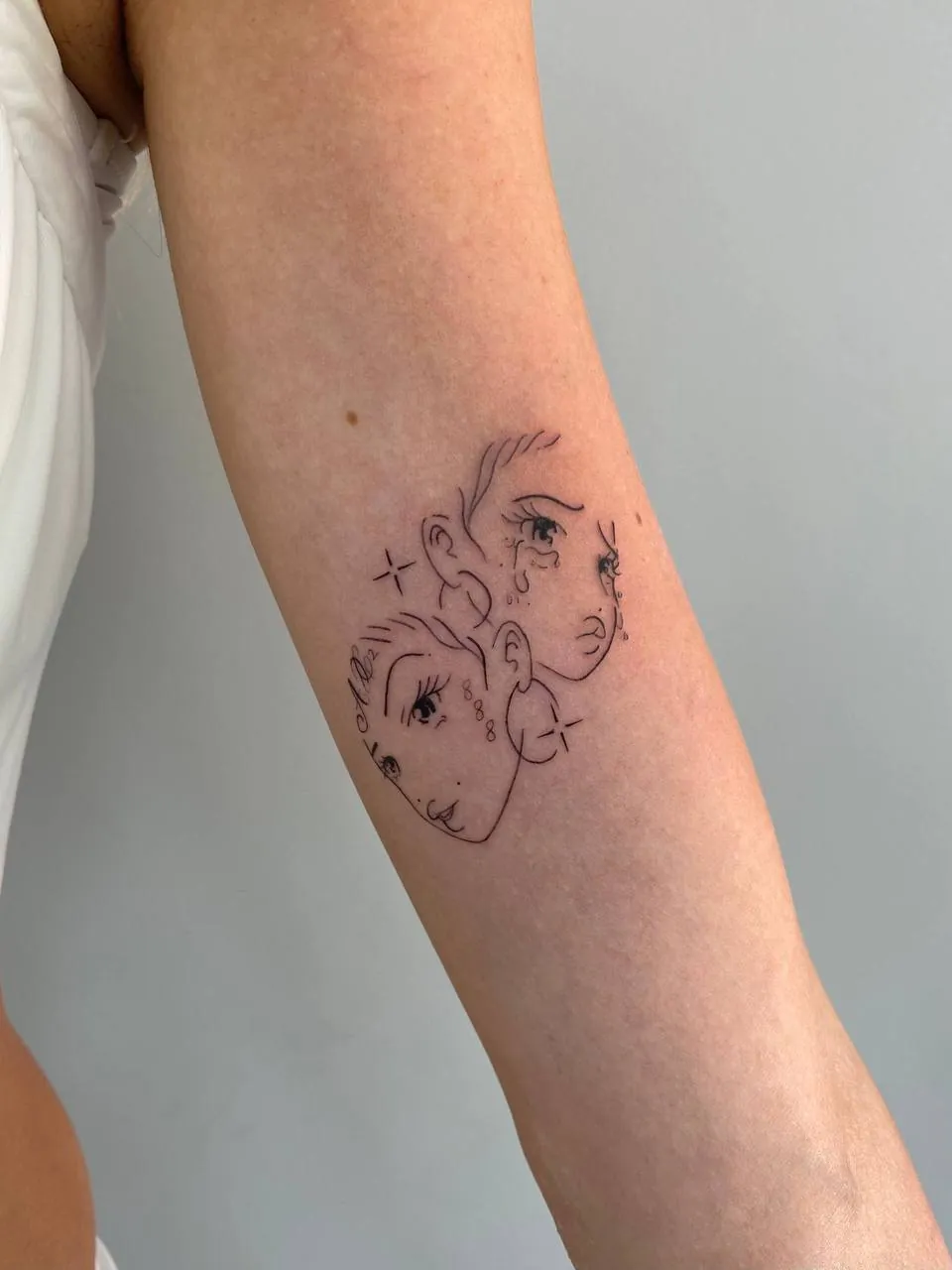 Fine-line tattoo of two faces on the inner upper arm